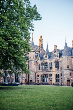 Glasgow Üniversitesi 'nin tarihi avlusunda, eğitim, miras ve doğa temaları için ideal büyük bir ağaç ve modern heykel manzarası