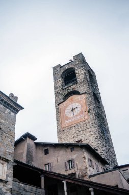 İtalya 'nın Bergamo kentindeki tarihi Torre Civica Campanone, büyük dekoratif saat yüzlü ve taş mimarisi eski kasaba binalarının üzerinde yükseliyor.
