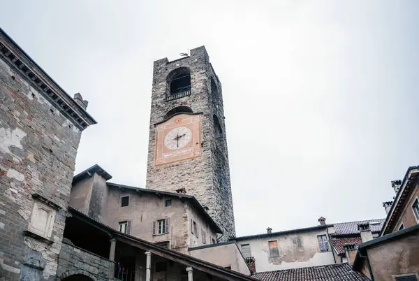 İtalya 'nın Bergamo kentindeki tarihi Torre Civica Campanone, büyük dekoratif saat yüzlü ve taş mimarisi eski kasaba binalarının üzerinde yükseliyor.