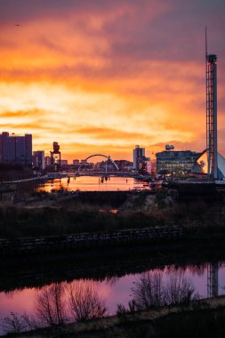 Glasgow, İskoçya 'daki Clyde Nehri üzerinde canlı bir günbatımı, Finnieston Crane, Clyde Arc ve SEC binaları da dahil olmak üzere simgesel simgelerden oluşan siluetler