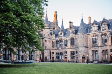 Glasgow Üniversitesi 'nin tarihi avlusunda, eğitim, miras ve doğa temaları için ideal büyük bir ağaç ve modern heykel manzarası
