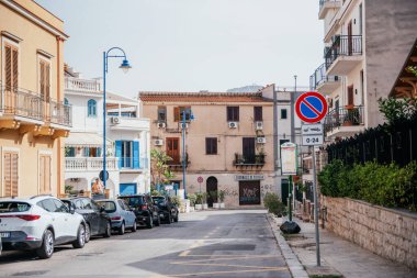 Sicilya, Palermo 'da sakin bir cadde. Geleneksel Akdeniz binaları, park edilmiş arabalar ve güneşli bir gökyüzünün altındaki uzak dağ manzarası.