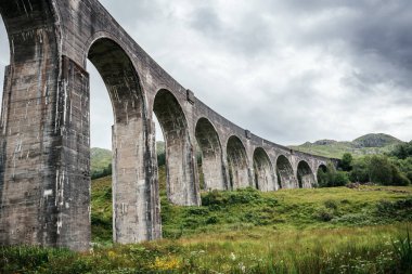 Harry Potter 'da sergilenen ikonik Glenfinnan Viyadük' ünün altında İskoçya Dağları 'nda büyük taş kemerler ve kayalık bir akarsu, seyahat, film ve manzara temaları için ideal.