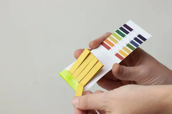 PH test şeritleri ve renk grafiği tutan eller