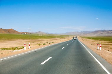 Moğolistan 'ın Ulgii kenti yakınlarında asfalt yolu olan bir manzara. Yoldaki ayırt edici Rus off-road aracı.