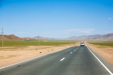 Moğolistan 'ın Ulgii kenti yakınlarında asfalt yolu olan bir manzara. Yoldaki ayırt edici Rus off-road aracı.