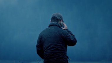 Adam dışarıda, yağmurda telefonla konuşuyor.