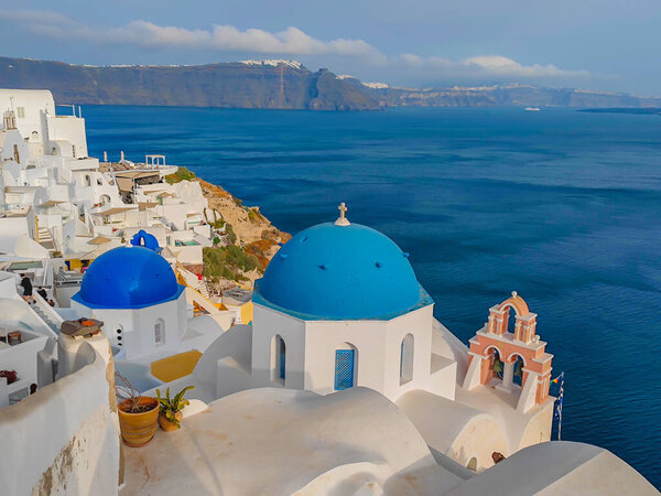 Панорамный вид на церковь Агиос Николаос в городе Ия в Санторини. Традиционные и известные белые дома и церкви с голубыми куполами в Эгейском море