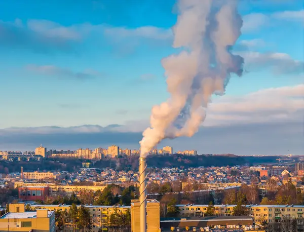 Aerial drone view of pollution in a city. White smoke coming from an industrial chimney located in center of large city with residential areas around.