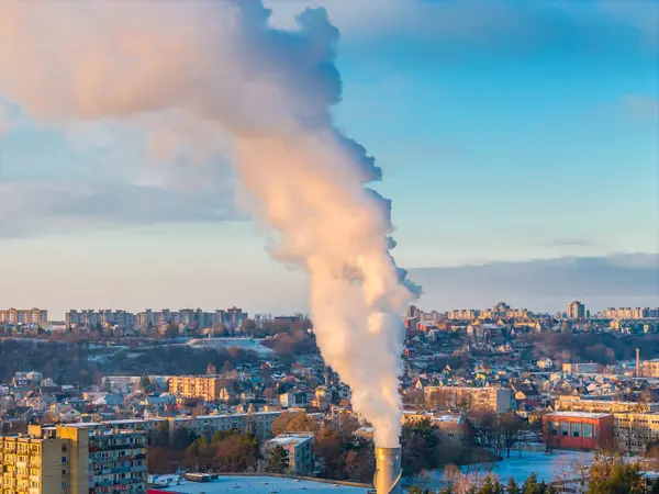 Aerial drone view of pollution in a city. White smoke coming from an industrial chimney located in center of large city with residential areas around.
