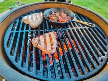 Kamado yumurtalı barbekü ızgarası. Ev terasında duruyor. Kavrulmuş ton balığı bifteği ve dökme demirde taze sebzeler var. 