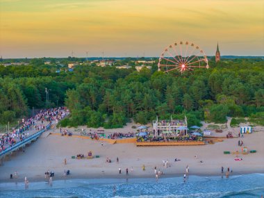 Akşamları plajın yanındaki şehirde ağaçların arasında dönme dolap. Hava aracı günbatımı fotoğrafı, Palanga, Litvanya