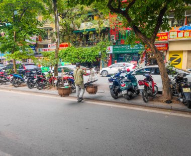 1227 2024 Hanoi, Vietnam. Vietnamlı sokak satıcısı. Vietnam sokaklarında meyve dolu sepetlerle yürüyen bir adam.