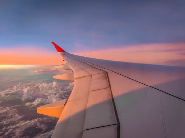 Uçak penceresinden bulutlara ve uçuş sırasında gün batımına kadar olan manzara. Kalın renkli bulutların üzerinde uçak kanadı. 