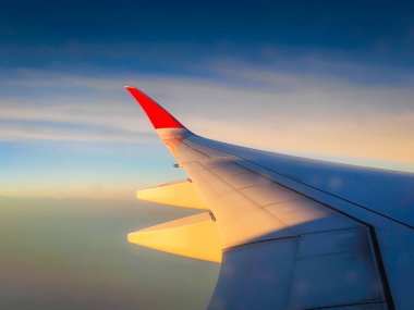 Uçak penceresinden bulutlara ve uçuş sırasında gün batımına kadar olan manzara. Kalın renkli bulutların üzerinde uçak kanadı. 