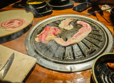 Kore barbekü tarzı restoran. İçinde ızgara olan geleneksel Kore yemek masası. Domuz eti ve sığır eti kömür ocağında ızgaraya hazır.