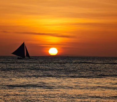 Boracay adası gün batımı manzaralı ve ufukta yelkenli var. Filipinler 'in deniz sularında altın bir saat boyunca inanılmaz günbatımı