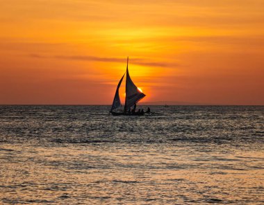 Boracay adası gün batımı manzaralı ve ufukta yelkenli var. Filipinler 'in deniz sularında altın bir saat boyunca inanılmaz günbatımı