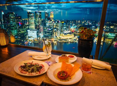 Singapur 'da lüks bir akşam yemeği, Marina Körfezi ve Singapur silueti manzaralı. Gökdelen Lokantası çarpıcı manzaralı şık bir yemek.