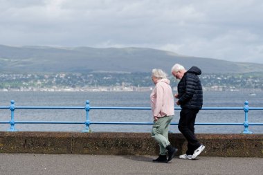 Yaşlı bir çift sahilde birlikte yürüyor.