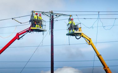 Tepedeki elektrik direkleri üzerinde çalışan adamlar.