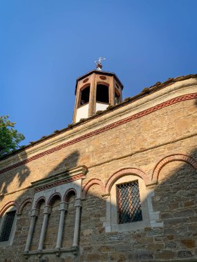 The weathered stone facade of the Saint Nikola church in Dryanovo, Bulgaria, with its distinctive arched windows and a small belfry, evokes a sense of timeless beauty and historical significance.  clipart