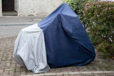 Motosiklet mavi gri koruyucu ile korunuyor. Şehrin sokak motosikletinde gümüş kaplama branda ceketli.