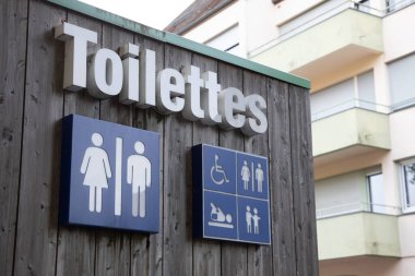 Tuvaletlerin Fransızca metni, ahşap binanın ön cephesinde tuvalet işareti simgesi anlamına gelir.