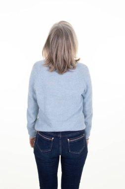 Middle aged senior woman wearing blue sweater and blue jeans trousers on a white background Rear grey hairs lady back view