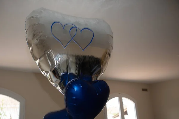 Blue silver heart shaped balloons inflated with helium on the ceiling of the room during the party