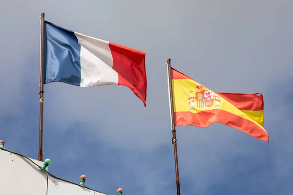 Spanish flag with France flag waving over cloud blue french spanish sky