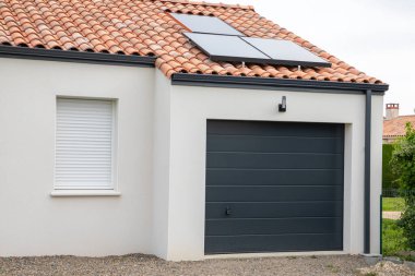 Modern ev cephesi kapalı garaj kapısı perdesi ve çatıda güneş paneli olan özel bir evin girişi.