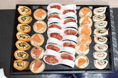 Different petit four and savory rolls on a platter for a party on grey table in top view