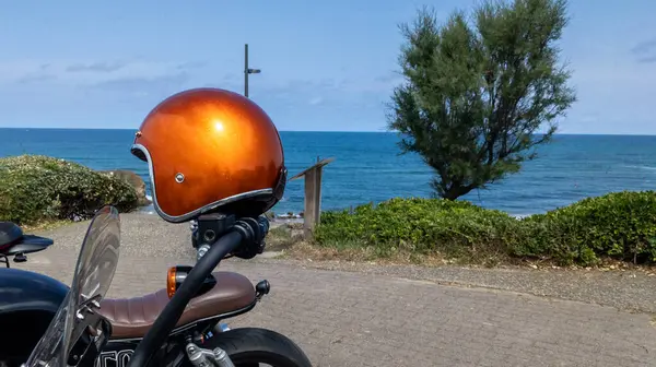 glittery orange motorcycle helmet placed on a motorbike parked on the seafront with the ocean on the horizon concept motorcyclist traveling