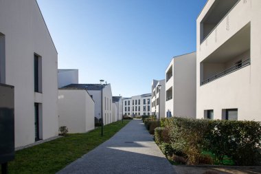 Temiz mavi gökyüzünün altında yeşil çimlerle çevrili, beyaz duvarları olan modern apartmanlar.
