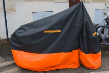Motosiklet, sokak kentindeki scooterların yanına park edilmiş turuncu siyah koruyucu muşamba kaplı.