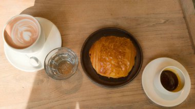 Çikolatalı Fransız kruvasanı ve beyaz bir fincan kahve ev içinde, su bardağı ve sıcak çikolatalı.