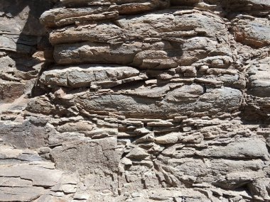 Gri ve kahverengi tonlardan oluşan, pürüzlü ve dokulu bir taş maddesinin küçük çakıl ve taşlarla birleştirilmiş, pürüzlü ve yıpranmış yüzeyine dağılmış küçük çakıl ve taşlardan oluşan yakın çekim görüntüsü..