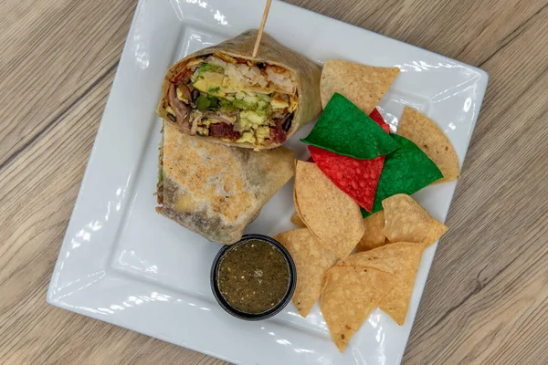 Overhead view of loaded breakfast burrito is cut in half to show the layers of eggs, bacon, and vegetables wrapped in a flour tortilla.
