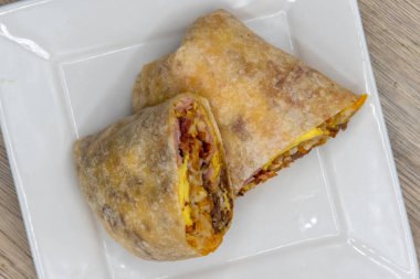 Overhead view of meat breakfast burrito with eggs, potatoes, baccon, and sausage all wrapped in a grilled flour tortilla to eat.