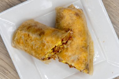Overhead view of traditional breakfast burrito with eggs, potatoes, salsa, and cheese all wrapped in a grilled flour tortilla to eat.