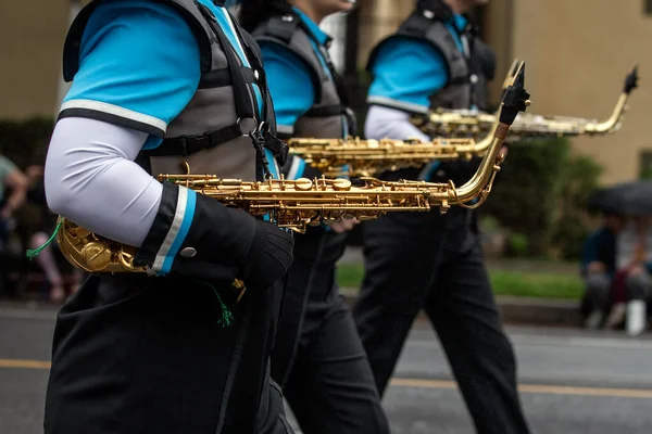 游行乐队的萨克斯风演奏者手戴着手套 一边拿着铜管乐器一边在街头游行 — 图库照片