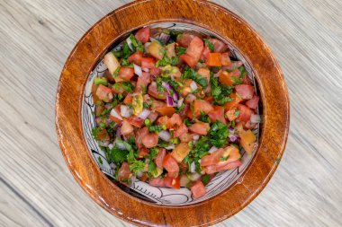 Meksika mutfağı sunumu için ahşap bir kasede servis edilen taze yapılmış pico de gallo salsa sosunun genel manzarası..