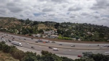 Los Angeles 'taki 405 otoyolu boyunca parçalı bulutlu gökyüzü ile kuzeye ve güneye giden araç trafiği sürekli ilerliyor..