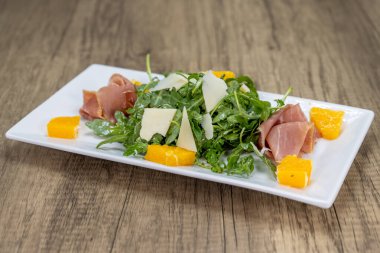 İtalyan salatası roka, parmesan peyniri, jambon ve portakal dilimleri bir tabakta..