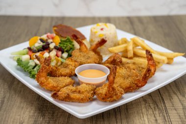 Lezzetli bir deniz mahsulü yemeği için patates kızartması ve salatayla servis edilen sosun etrafına yerleştirilmiş karides börekleri..