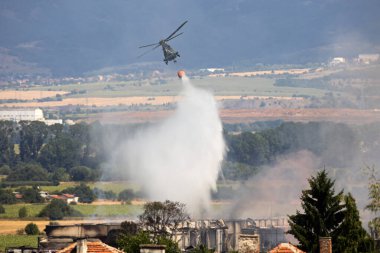 A military helicopter extinguishes fire on the ground with a helicopter bucket (helibucket). clipart