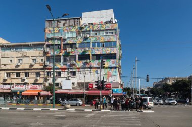 Netanya, İsrail - 11 Mart 2024: Arka planda grafiti kaplı bir bina bulunan insanlar caddeyi geçmek için trafik ışıklarında bekliyorlar