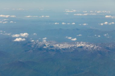 10.000 metre yükseklikten bulutların arasındaki karlı dağ zirvelerinin manzarası.