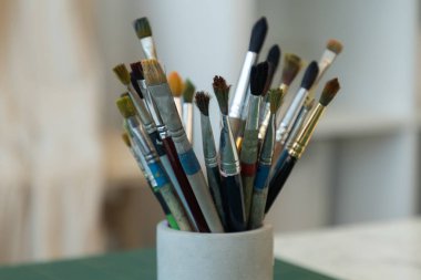 Suluboya, yağ ve akrilik fırçalar tek bir seramik bardakta toplanır, atölye ışığı altında yıkanır.